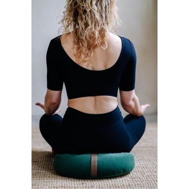 Kobieta w czarnym stroju siedzi na zielonej poduszce do medytacji, ujęcie od tyłu, styl boho.